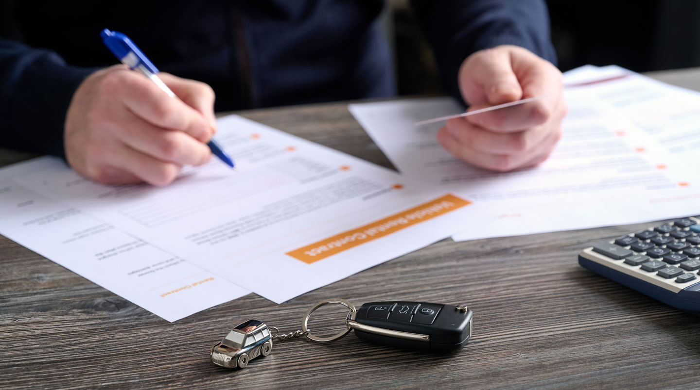 Close-up of hands reviewing vehicle rental contract document in French on desk with calculator and pen at rental agency counter